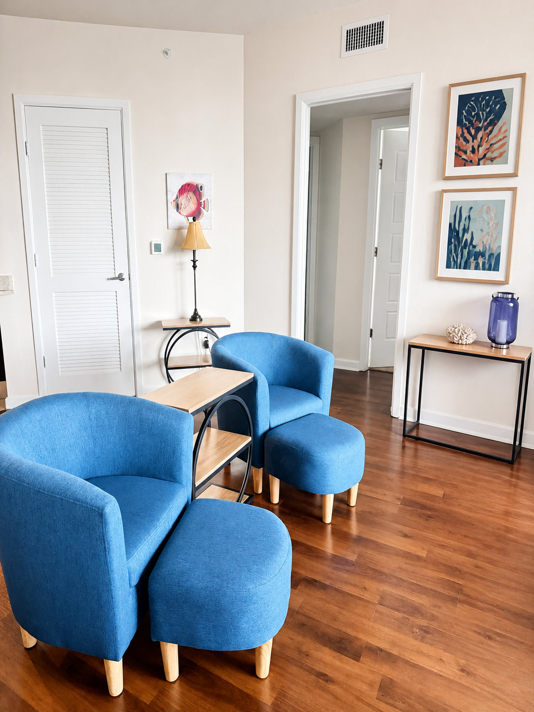 Living room with blue barrel chairs, hardwood floors, and coastal wall art